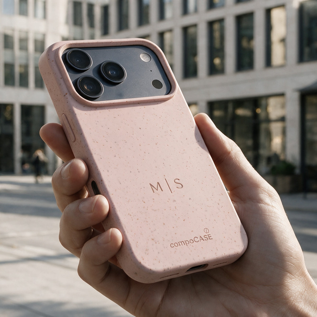 compoCASE Handyhülle in Soft Rose mit gravierten Initialen M|S in der Hand vor einer Stadtfassade